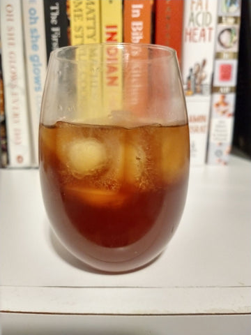 A glass of iced cold brew coffee sits on a shelf in front of a collection of cook books