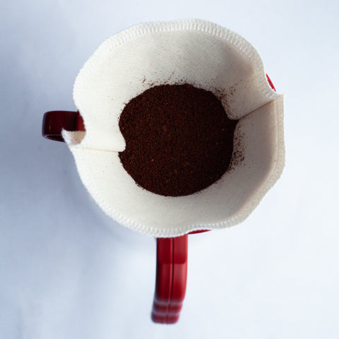 Birds eye view of a dry pour over dripper with coffee grinds inside sitting atop a red mug.