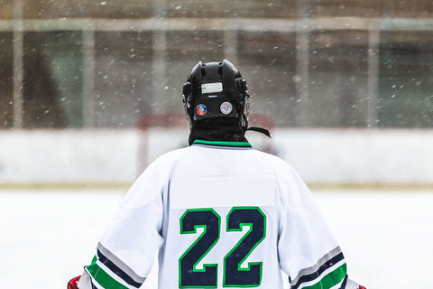 A hockey player stands on the ice with their back to the camera.