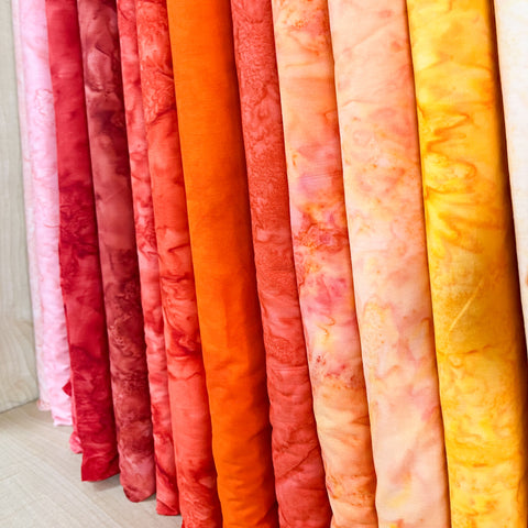 A row of orange, red and yellow batiks on the bolt