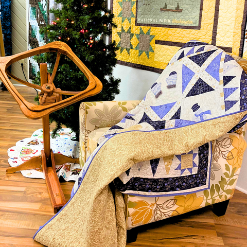 A blue and white winter quilt resting on an armchair next to a wooden quilting hoop