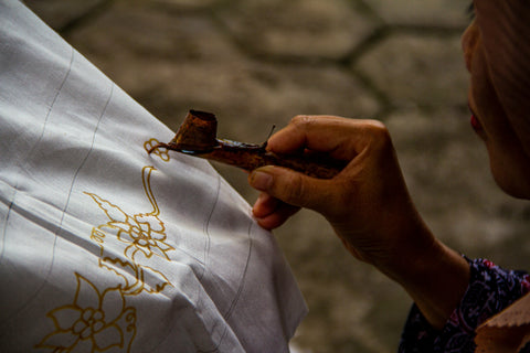 a woman hand canting a batik floral design