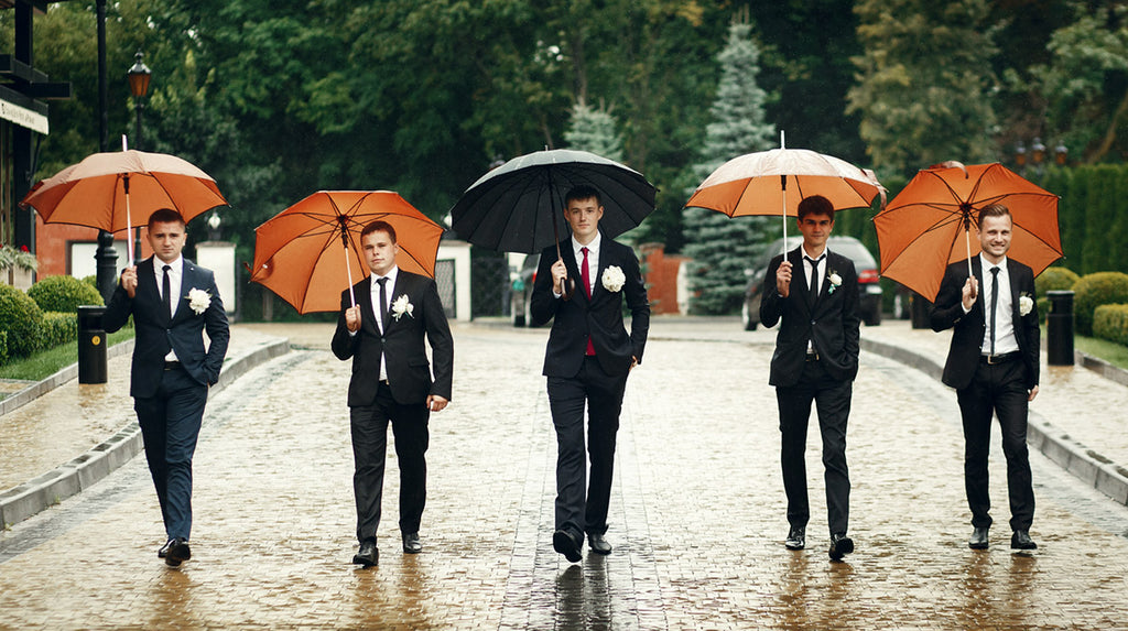Groomsmen walking in the rain holding orange umbrellas