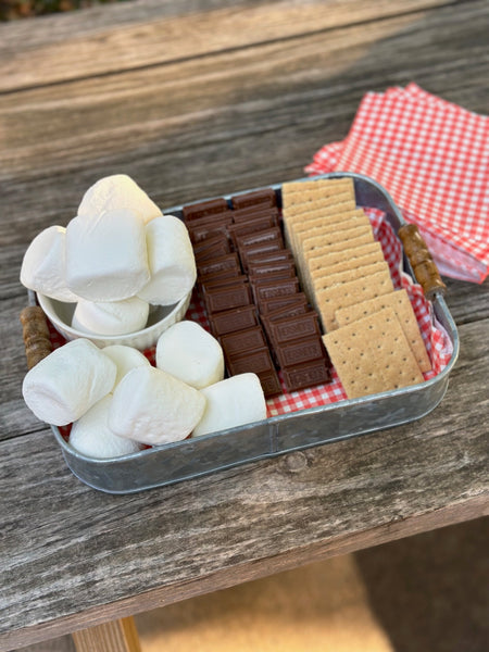 galvanized tray on picnic table holding s'mores items and red checkered napkins