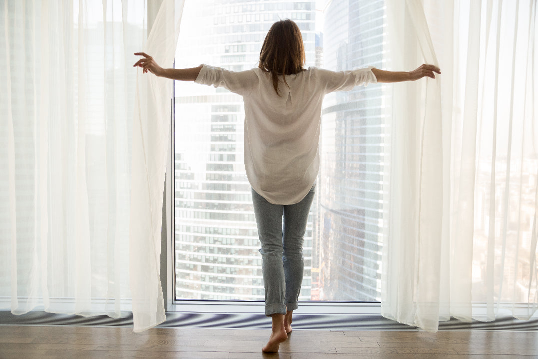 Woman in front of window opening curtains