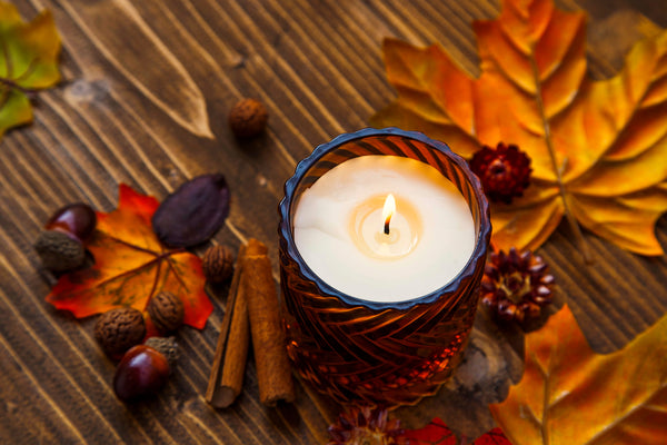 fall candle with leaves, cinnamon sticks, and acorns on a wooden surface