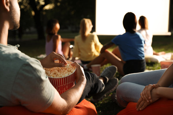 Adult friends gathered on cushions, eating popcorn and enjoying an outdoor movie