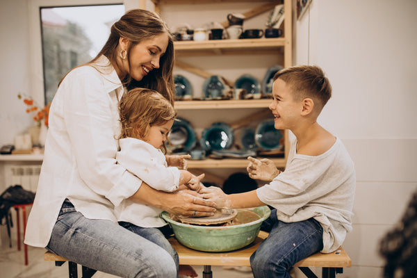 Mother and two children smiling while turning a pottery wheel together