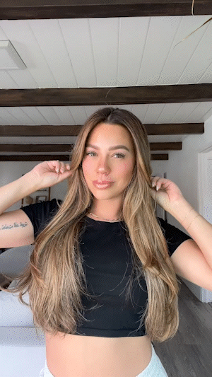 A woman in a black crop top playing with her long, wavy, light brown hair.