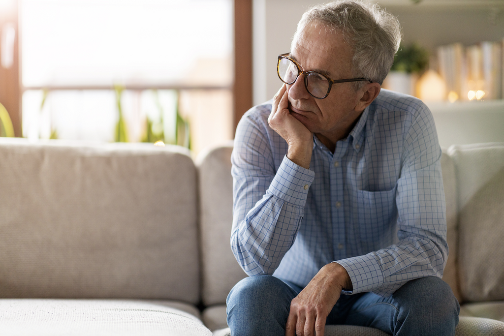 how do you handle stress: Elderly man sitting on a couch while deep in thought