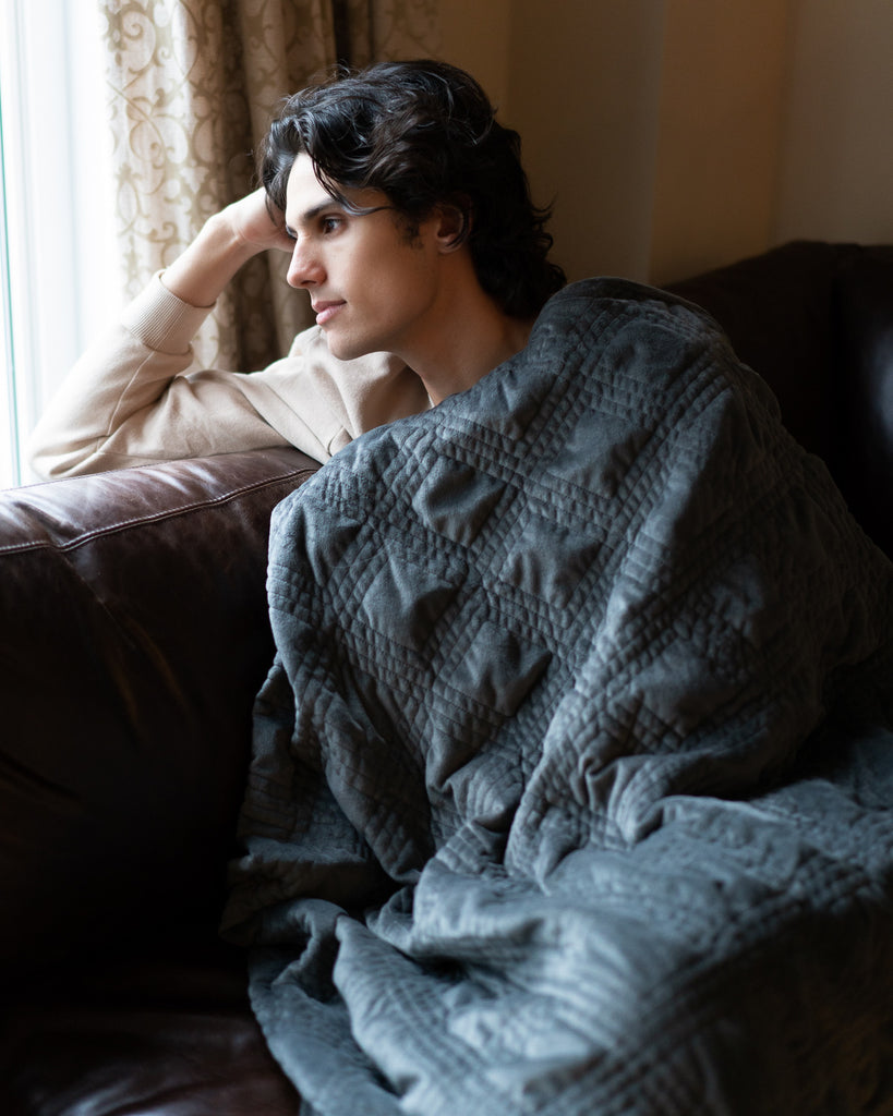 Man staring out the window while covered in a blanket