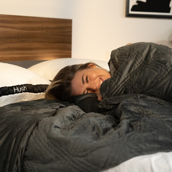 Smiling woman lying in bed with Hush pillows and weighted blanket