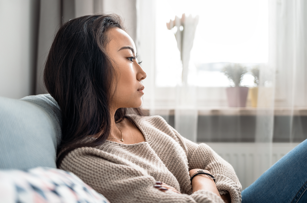 how do you handle stress: Woman sitting on a couch with her arms crossed while deep in thought