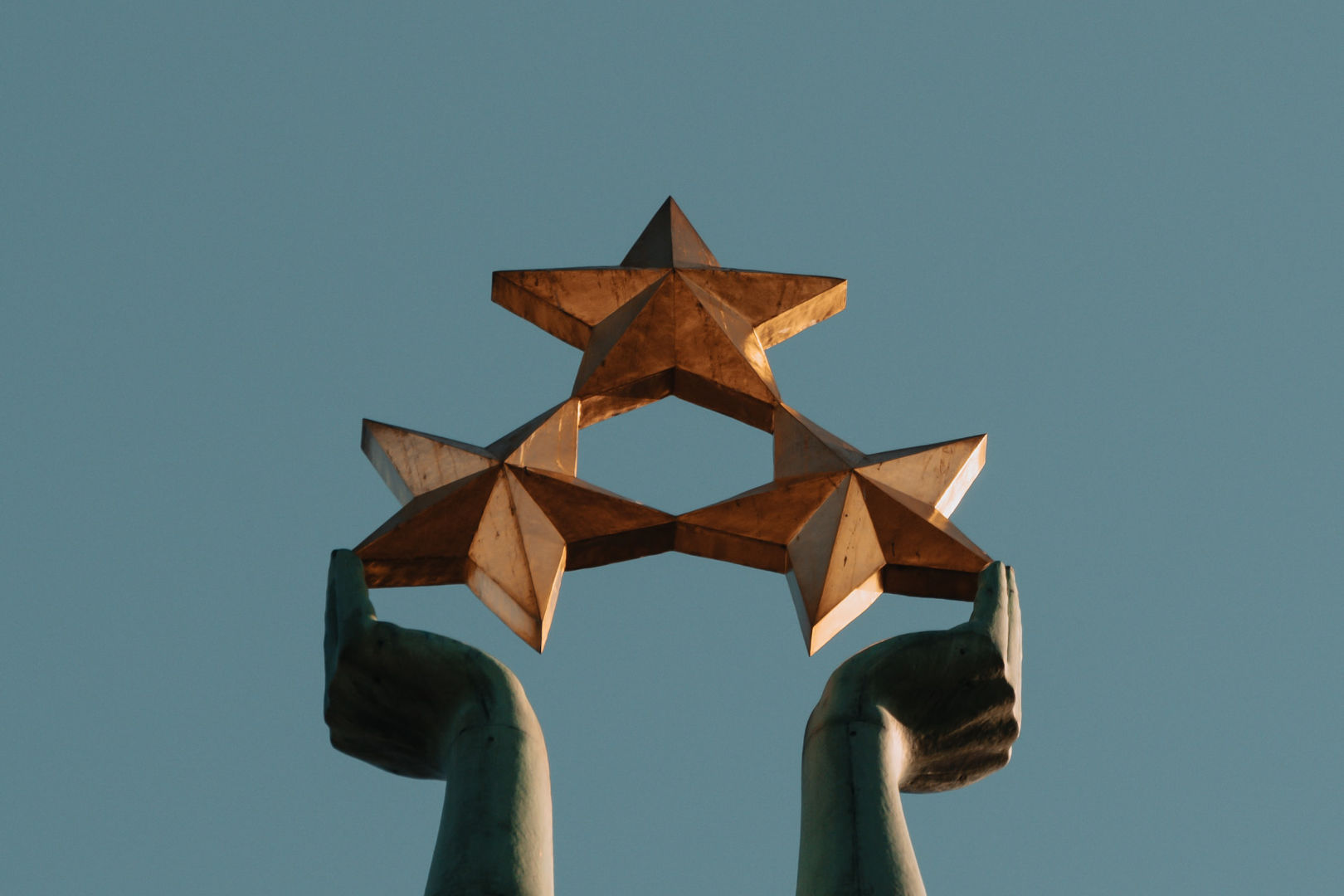 A brown infrastructure showing hands holding up a 3-star design under clear blue sky.