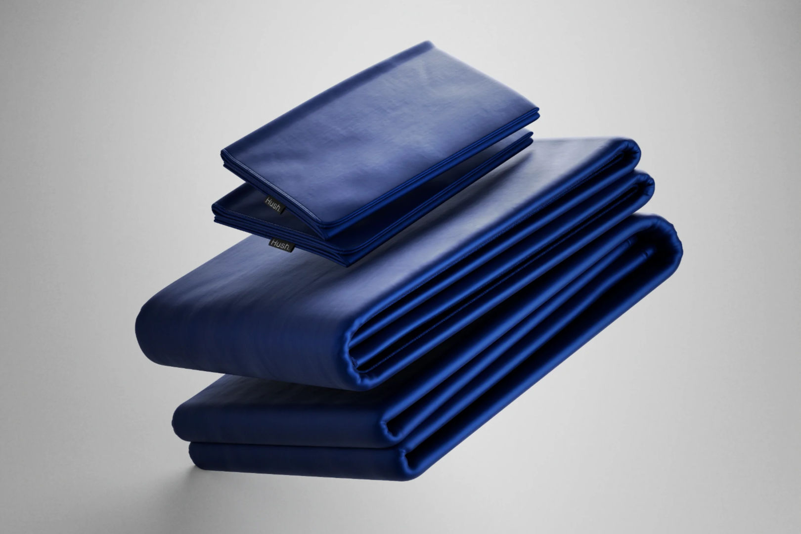 A set of neatly folded Hush Iced 2.0 Bamboo Cooling Sheet and Pillowcase in navy blue color in a light grey background.