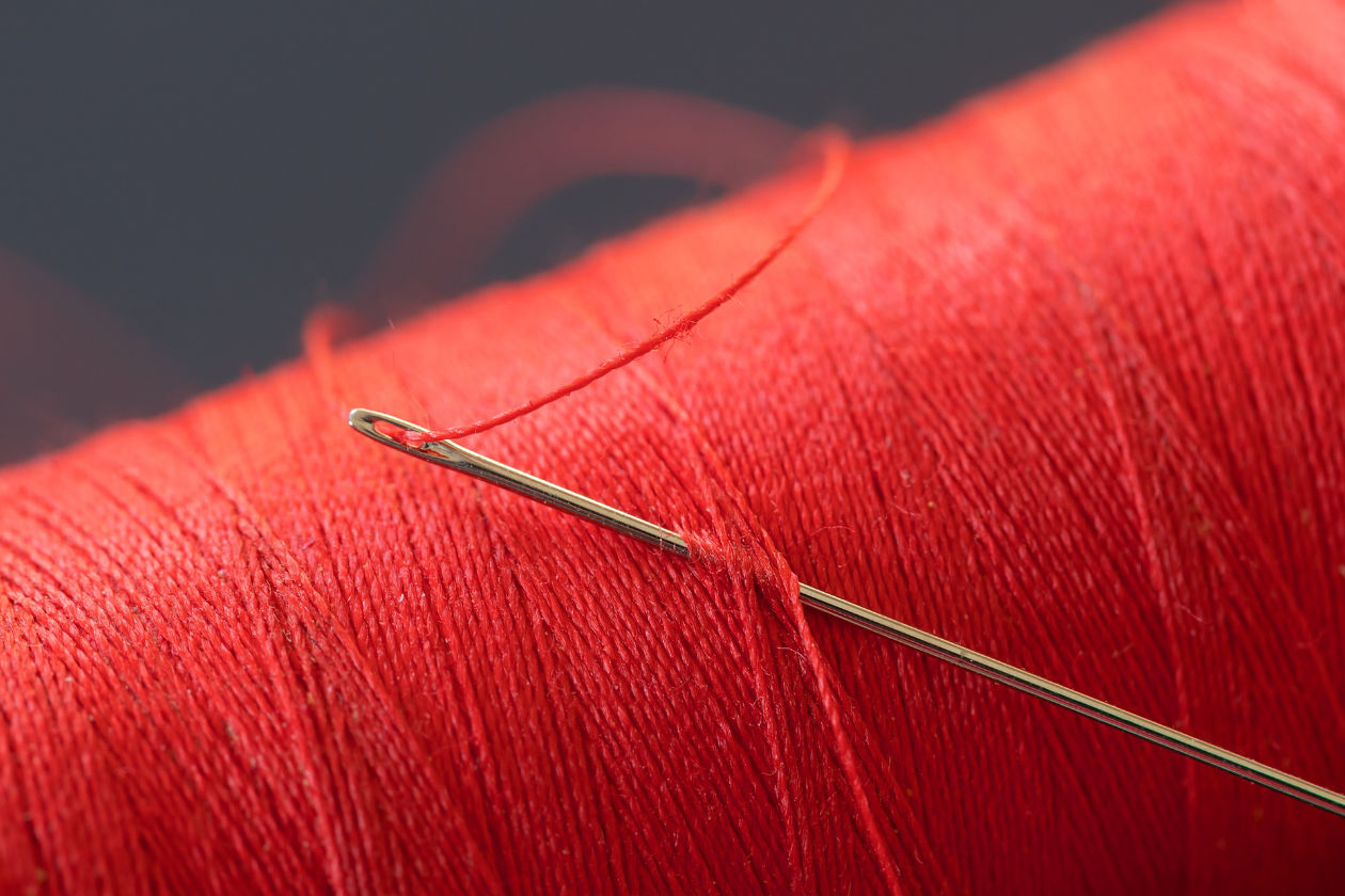 A spool of red thread with a needle inserted in it.
