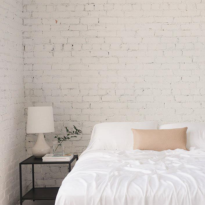 A bed with Cozy Earth bamboo sheets on them. A table with a lamp and decorative plants on it sits next to the bed.