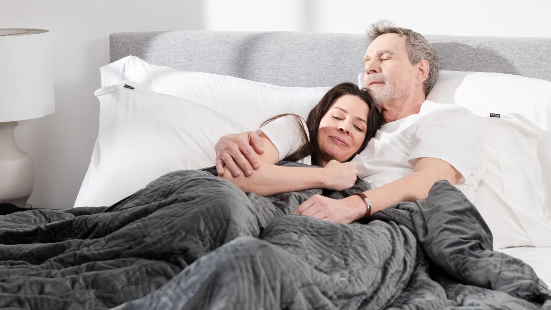 A loving couple cuddling under a Hush weighted blanket.