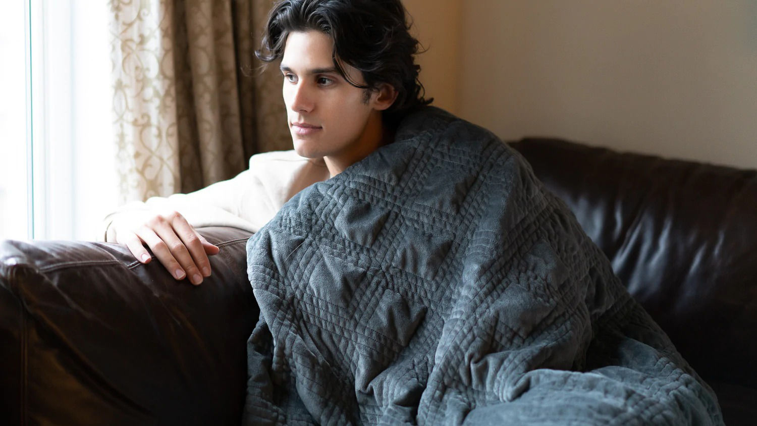 Man sitting on a couch with a Hush Classic weighted blanket.