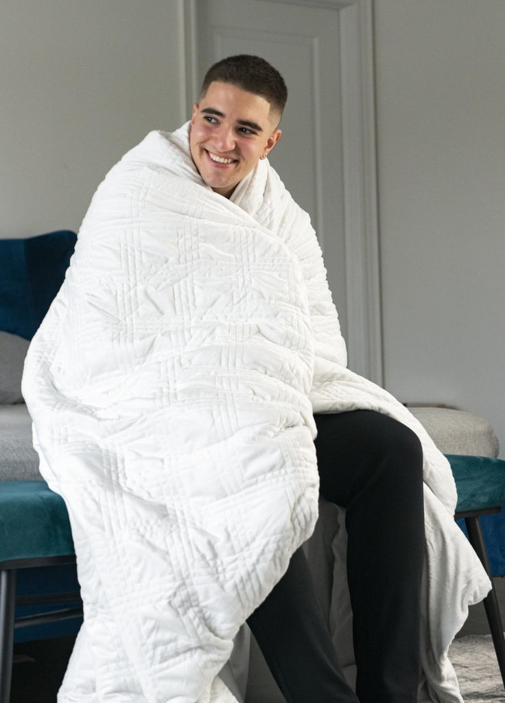 how to calm down: Smiling man sitting at the foot of his bed with a blanket wrapped around his shoulders