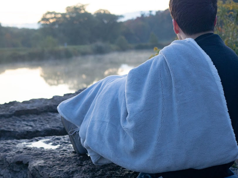 Man with a blanket over his shoulder looking over a lake