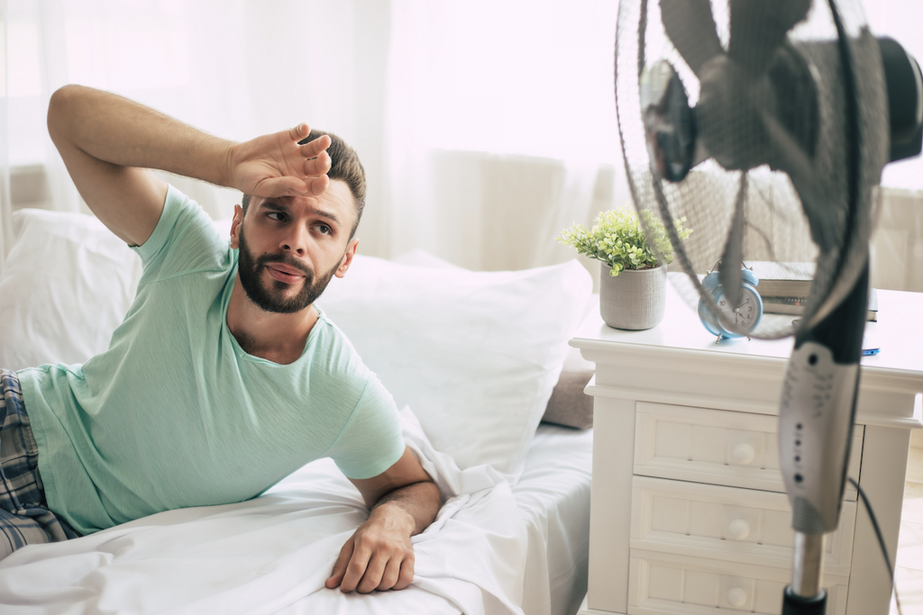 too hot to sleep: Man with his hand on his forehead and looking at the electric fan while in bed