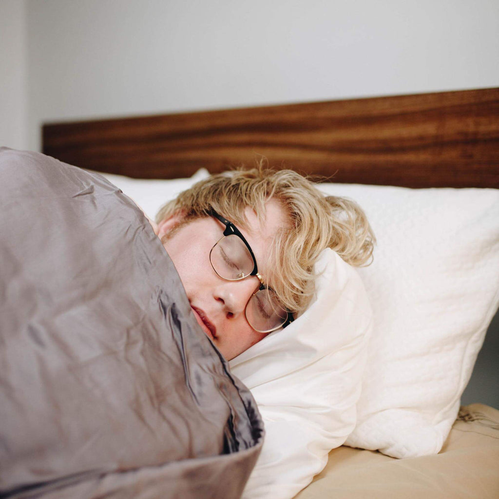 waking up tired: Man sleeping with a weighted blanket while wearing his eyeglasses