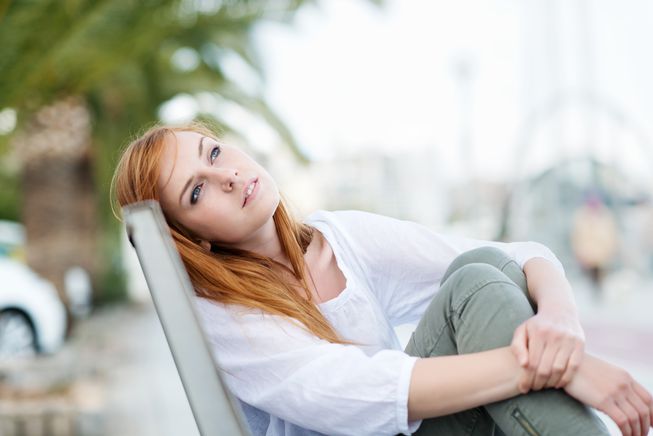 girl sitting down and holding her legs while looking at the sky
