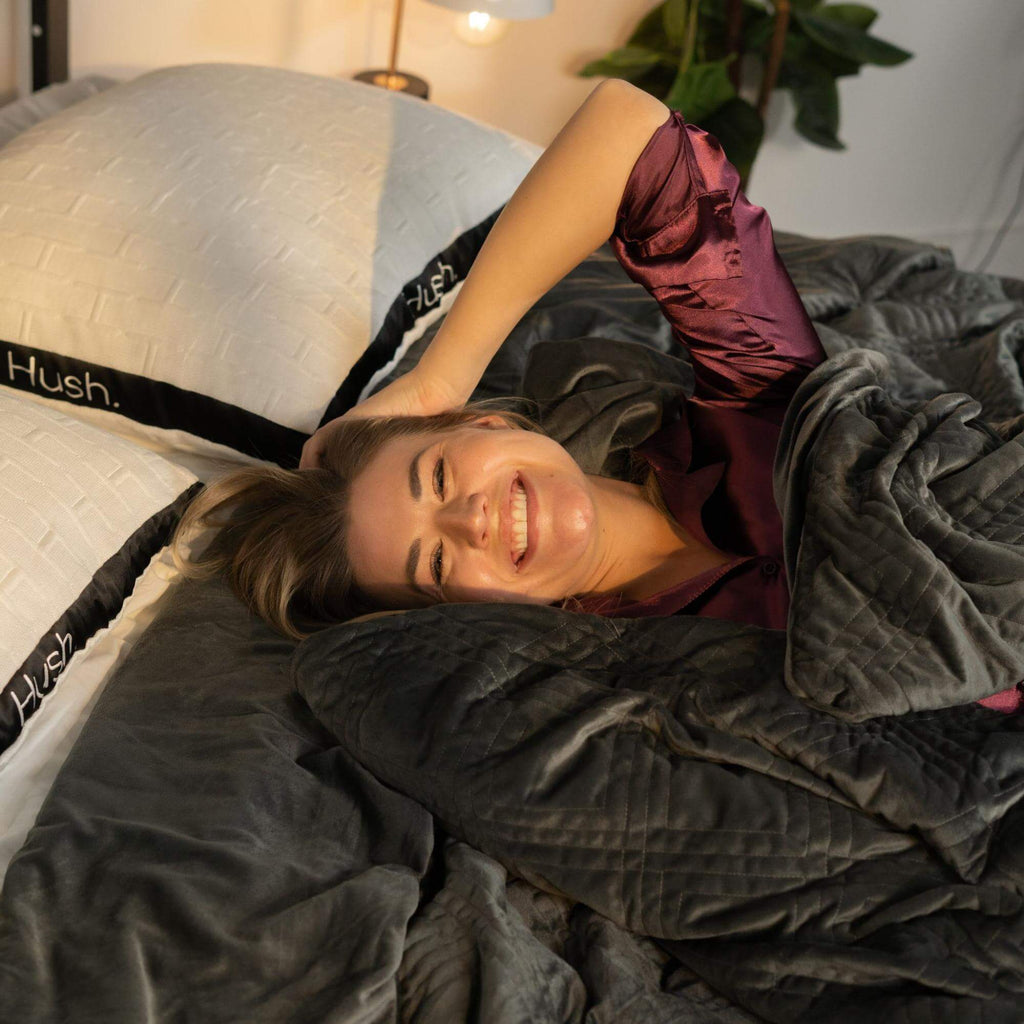 Smiling woman lying in bed with Hush pillows and weighted blanket
