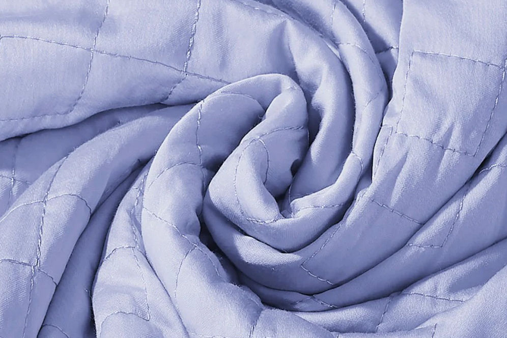 A Gravity cooling weighted blanket in periwinkle color curled up in center.