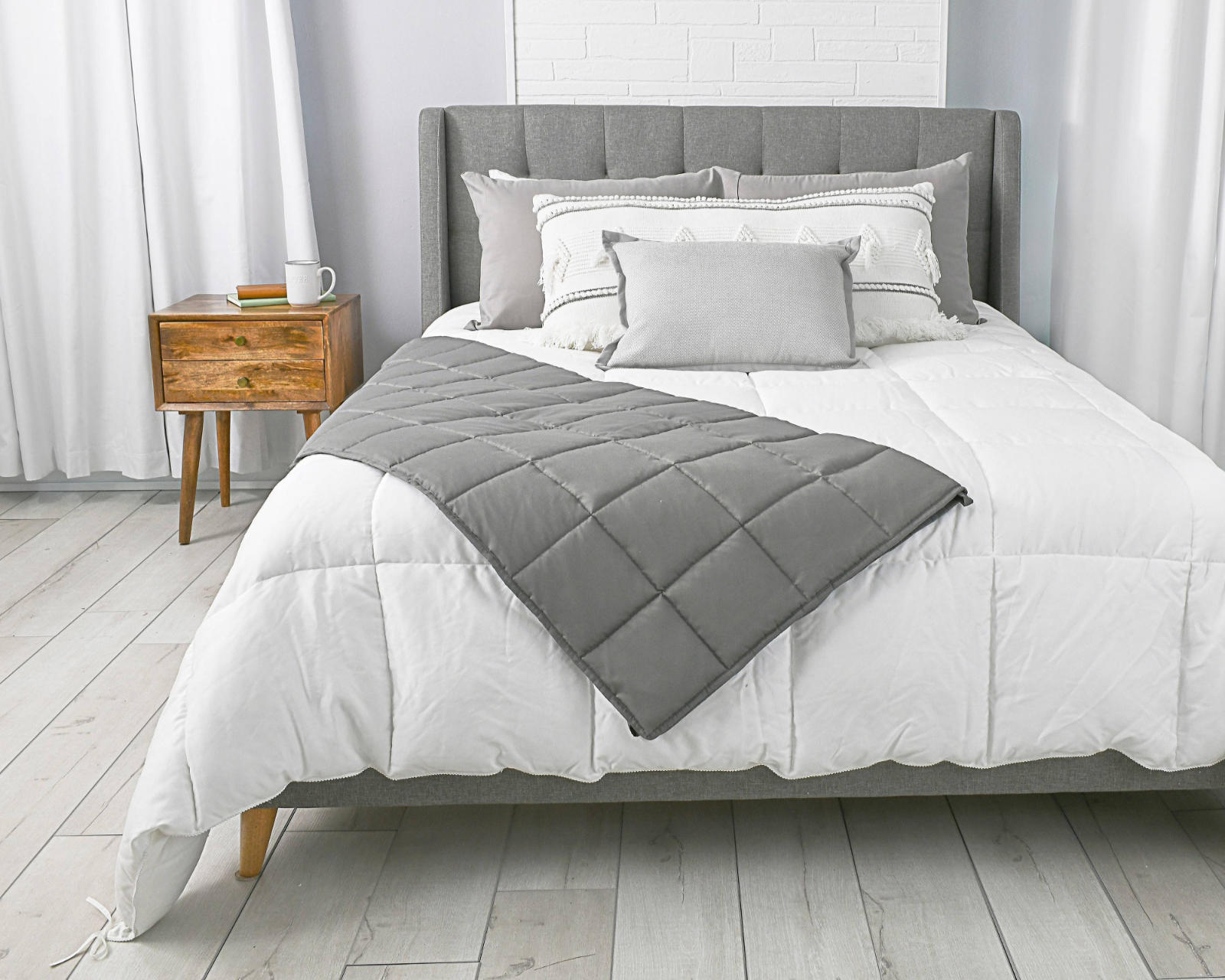 A bedroom with a gray Tranquility Essentials Weighted Blanket draped diagonally on the bed.