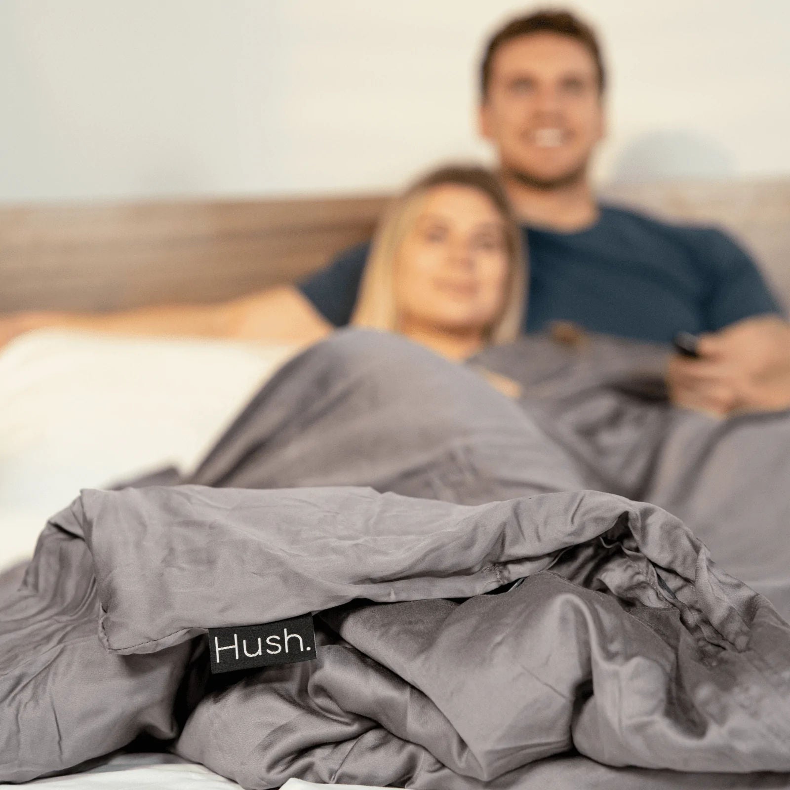 An out of focus couple under a Hush weighted blanket, with the tag saying “Hush” in focus.