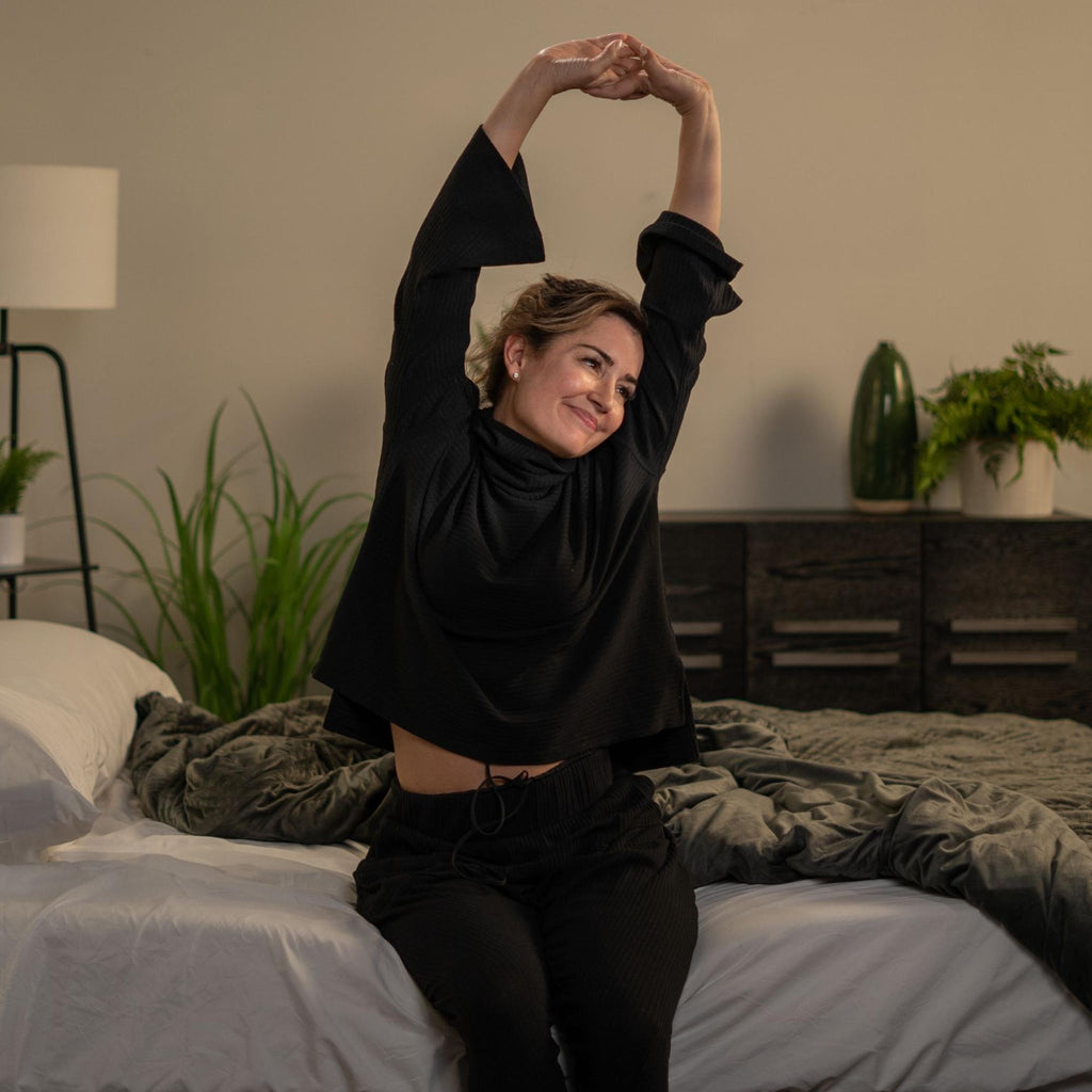 how to become a morning person: Smiling woman stretching while sitting in bed
