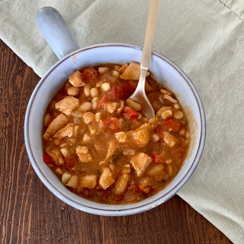 bowl of chicken chili on a wooden table with a light green cloth napkin nearby