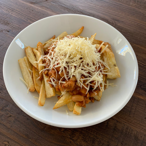 bowl of chicken chili over french fries with cheddar cheese on top over a wooden table