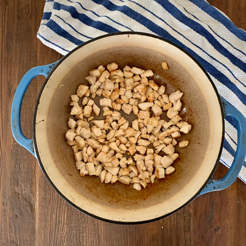 browned chicken pieces in a blue Dutch oven on top of a wooden table with a blue stripped towel in the corner