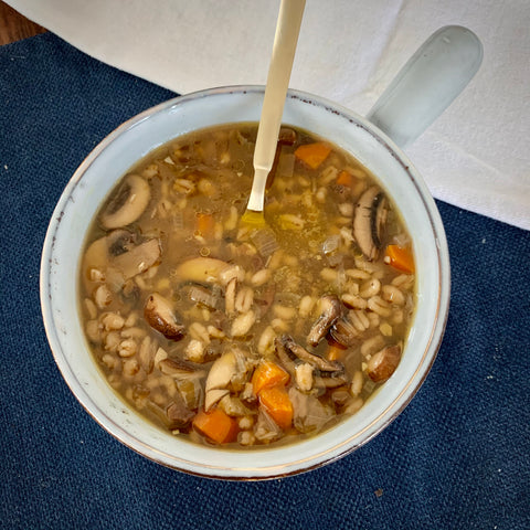 mushroom barley soup in a gray bowl with a golden spoon, on top of a blue placemat and white cloth napkin