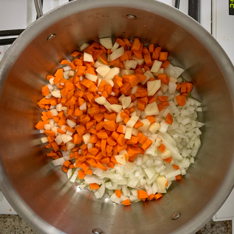 diced carrots and onions in a large all-clad pot ready to be sauteed for mushroom barley soup