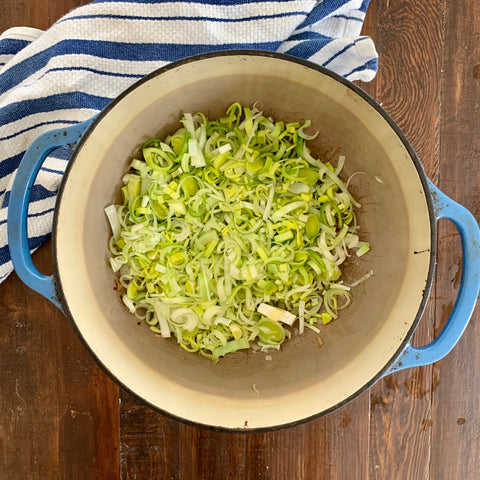 sliced leeks and minced garlic in a blue dutch oven for potato leek soup