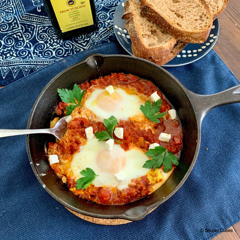 image of cooked shakshuka in a cast iron pan with 2 eggs, feta cheese, and parsley