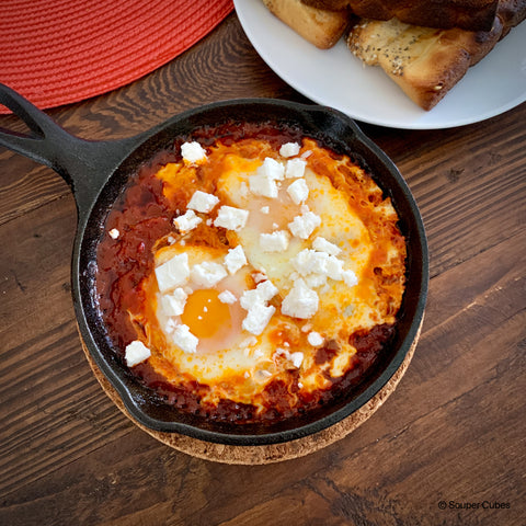 pan of shaakshuka with 2 eggs and feta cheese on a wooden table