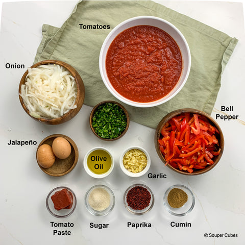overhead shot of ingredients for shakshuka, including: tomatoes, onion, jalapeno, eggs, bell pepper, cumin, olive oil, garlic, tomato paste, sugar, and paprika