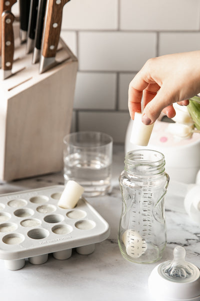 image of frozen breast milk being placed in a glass bottle near a mymilk tray