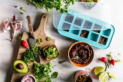Ingredients spread out on a kitchen table and cutting board with Souper Cube trays being used to store meals. 