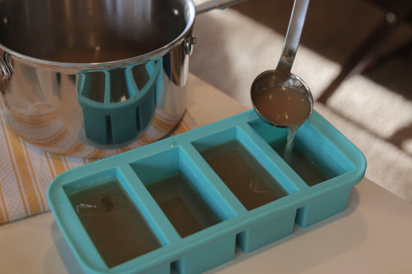 Soup poured from a pot into the Souper Cubes tray with a  lattle.