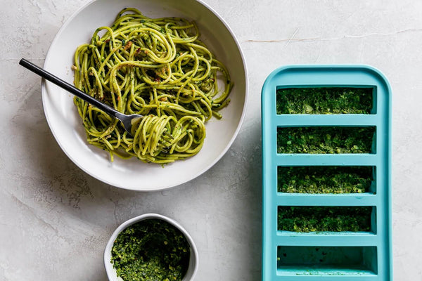 Cooked pasta in a bowl with a spoon accompanied by ½ cup Souper Cube trays.