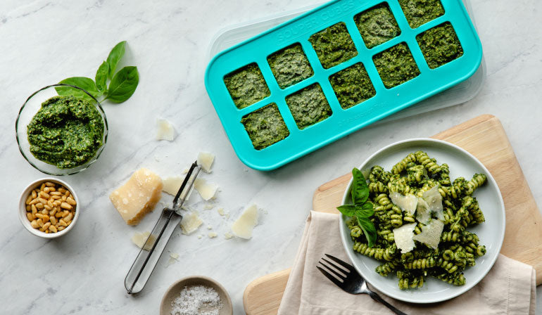 Pesto frozen in a Souper Cubes tray shown next to a dish of pasta covered in pesto.