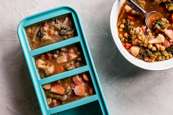 Frozen soup in a Souper Cubes tray with a white bowl of reheated soup beside it.