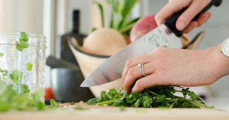 Close up of a person's hands chopping herbs.