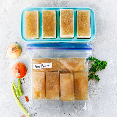 1-cup Souper Cubes tray at the top with frozen broth with 1-cup portioned broth cubes in a large Ziplock bag with a piece of masking tape labeled “bone broth”.